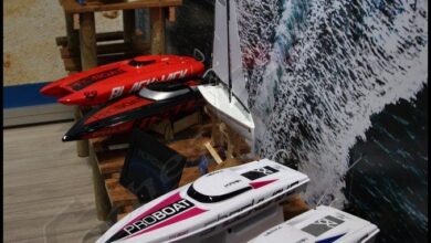 Varias lanchas de radiocontrol de casco blanco, rojo y verde junto a un velero, colocadas sobre soportes de madera en un expositor