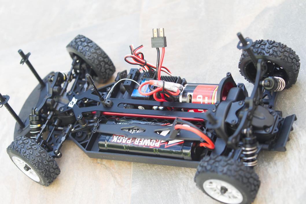 Chasis de un coche de radiocontrol de rally de tres cuartos, con la batería, el motor y el cableado a la vista