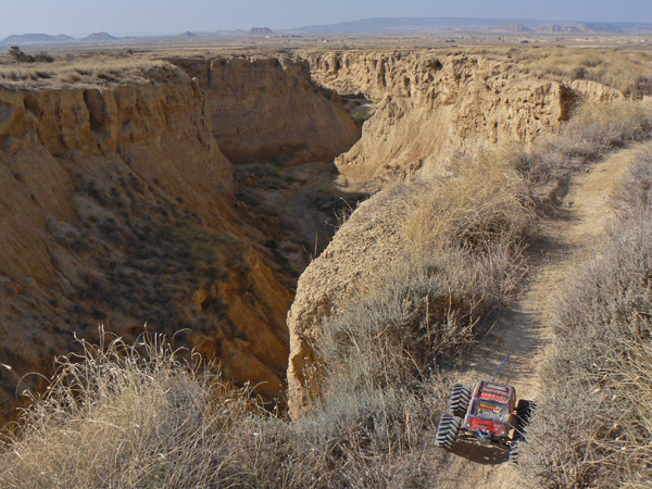 Coche de radiocontrol al borde de un barranco de tierra, con el paisaje árido de fondo