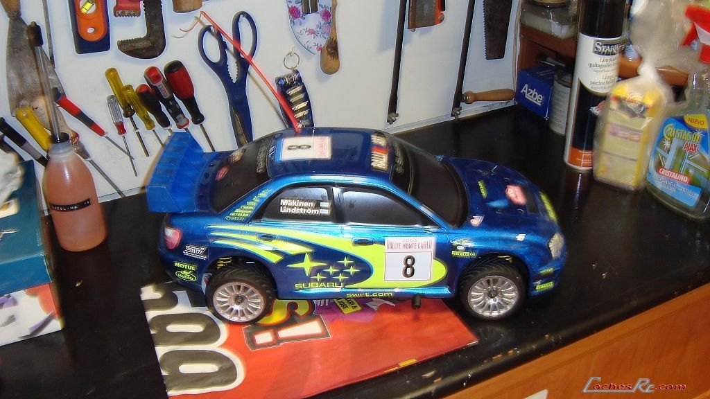 Coche de radiocontrol de rally con carroceria azul sobre la moqueta de un circuito