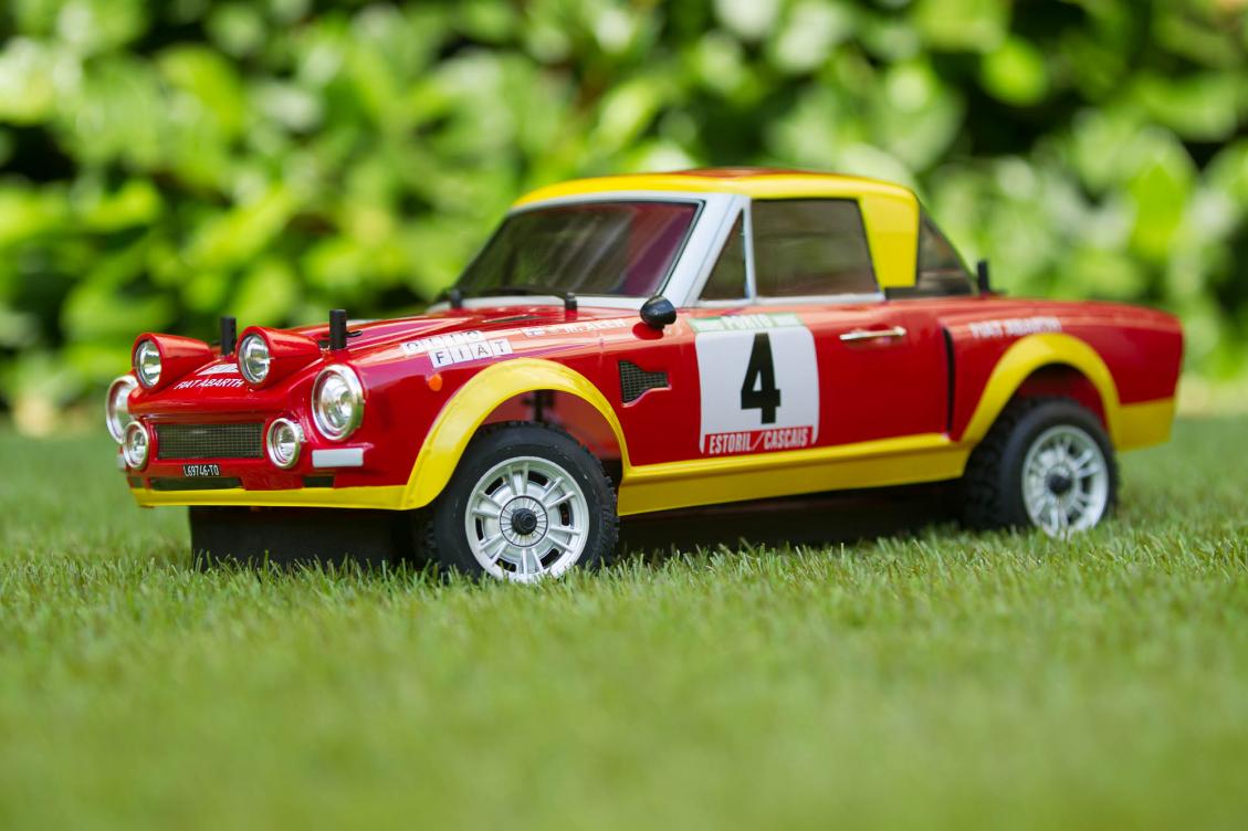 Coche de radiocontrol de rally con carrocería de Fiat 124 Abarth en rojo y amarillo, sobre hierba