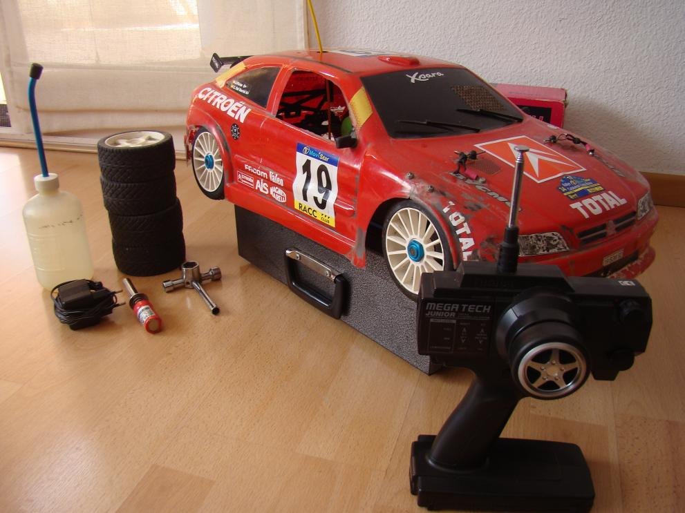 Coche de radiocontrol de rally rojo preparado junto a su emisora y sus ruedas de repuesto