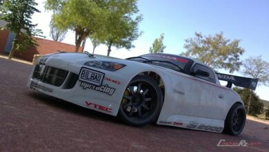 Coche de drift de radiocontrol con carroceria blanca de turismo japones, aleron trasero y llantas negras, visto de tres cuartos delantero