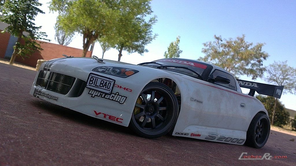 Coche de drift de radiocontrol con carroceria blanca de turismo japones, aleron trasero y llantas negras, visto de tres cuartos delantero