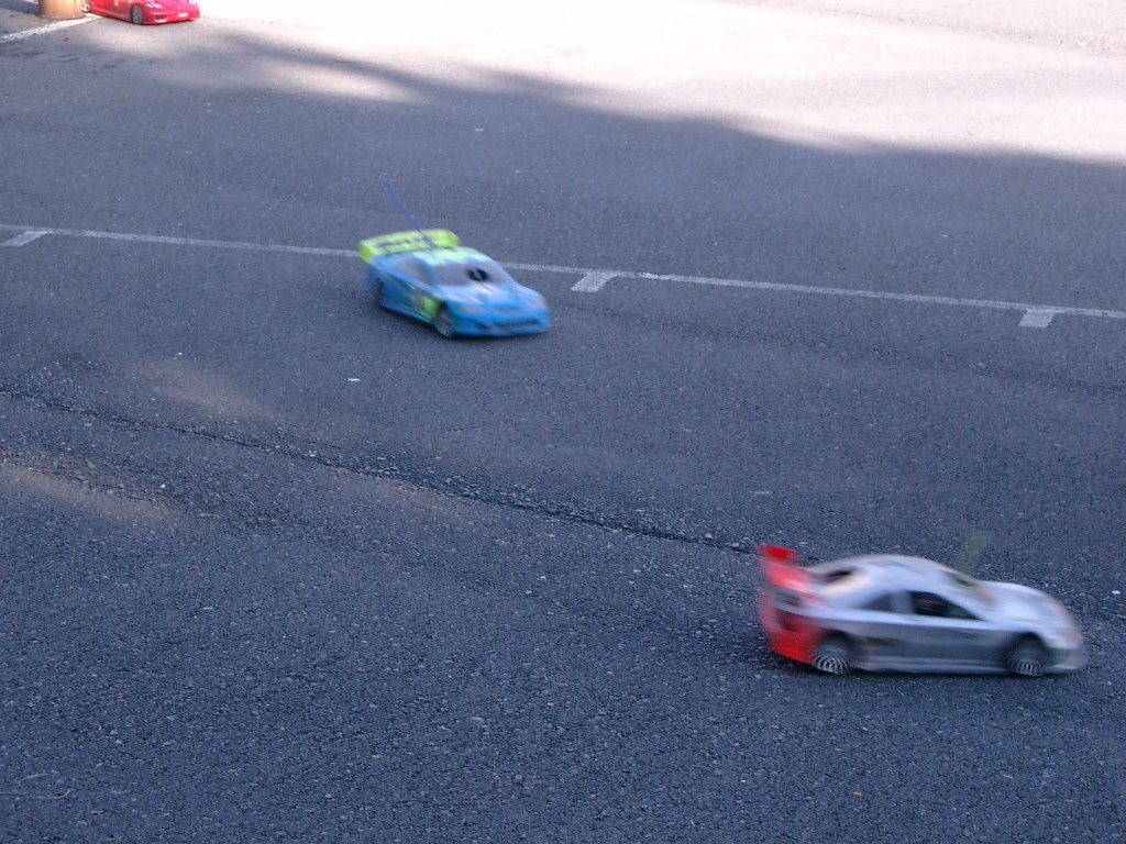 Coche RC de touring blanco y rojo rodando sobre asfalto