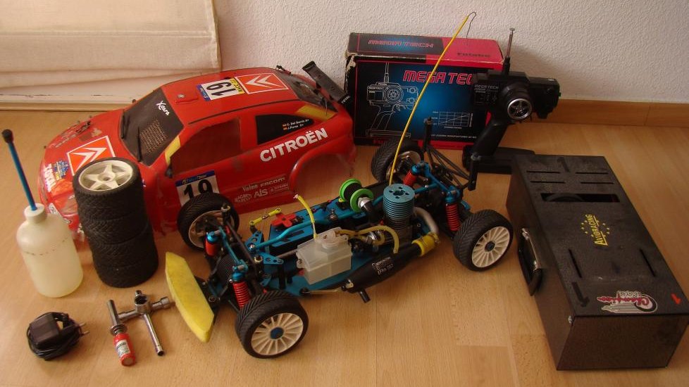 Dos coches de radiocontrol de rally con su emisora, botes de combustible y herramientas