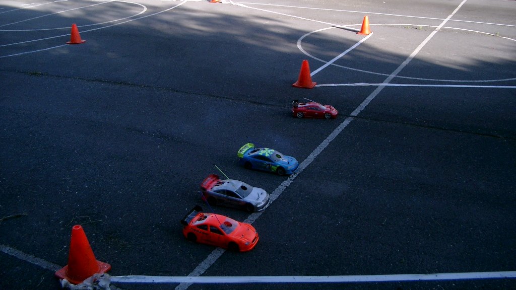 Varios coches RC de touring rodando sobre una pista de asfalto con conos