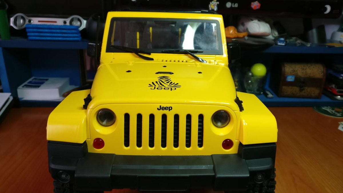 Crawler de radiocontrol con carrocería a escala de Jeep amarillo, visto de frente, con sus ruedas de tacos