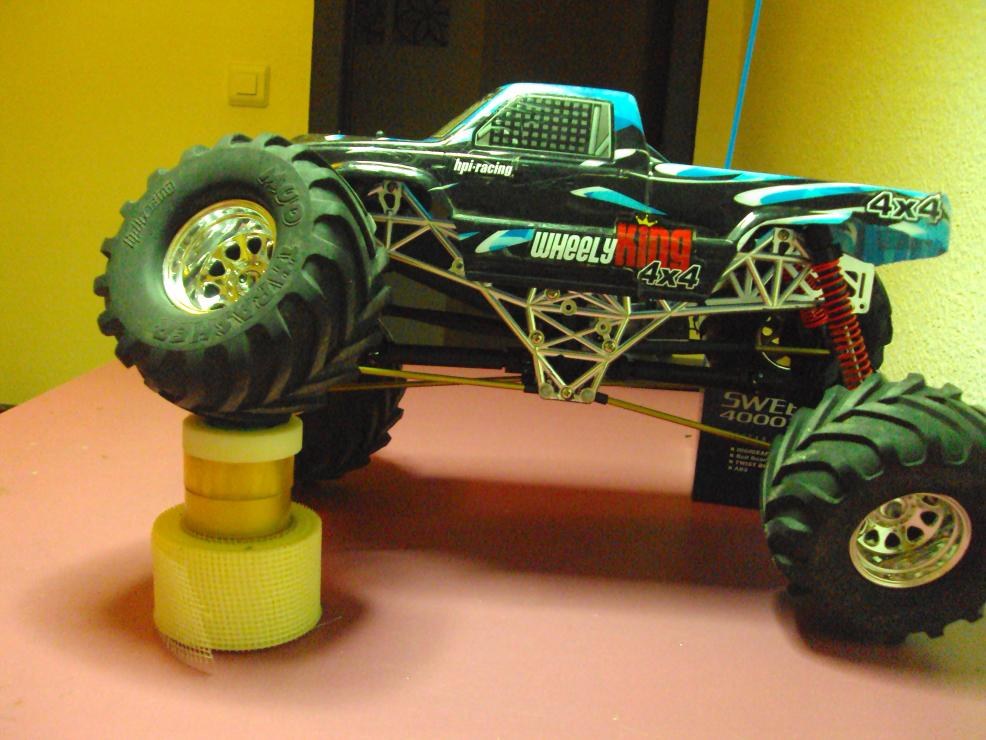 HPI Wheely King con una rueda delantera levantada sobre unos rollos de cinta, mostrando la articulación del eje rígido con las otras tres ruedas apoyadas
