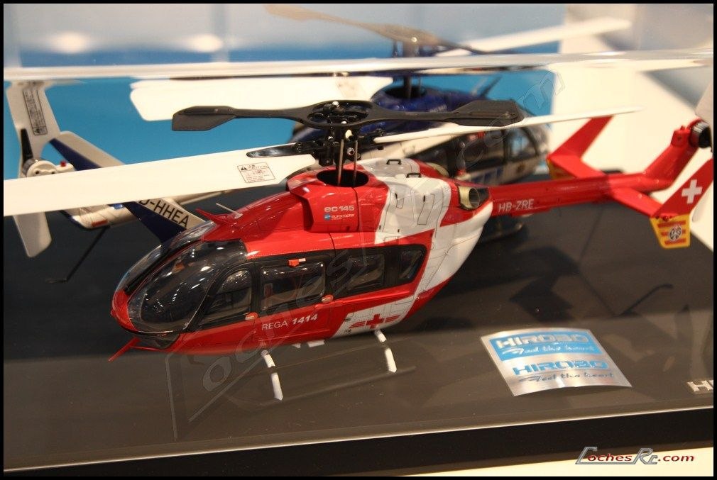 Helicoptero de radiocontrol a escala con carroceria roja y blanca de helicoptero de rescate, expuesto sobre una peana