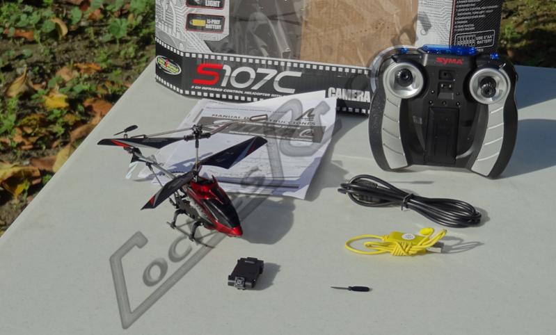 Helicóptero de radiocontrol con cámara junto a su emisora, el cable de carga y las palas de repuesto