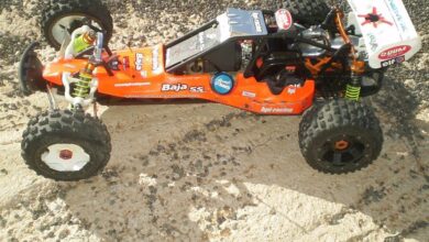 Buggy de gran escala HPI Baja 5B con carroceria naranja y blanca y neumaticos de tacos, sobre un terreno de tierra