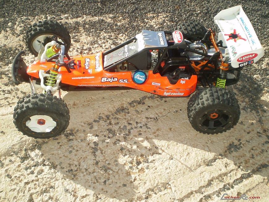 Buggy de gran escala HPI Baja 5B con carroceria naranja y blanca y neumaticos de tacos, sobre un terreno de tierra