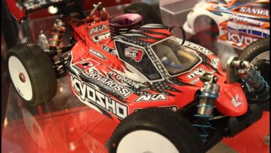 Buggy de radiocontrol de la marca Kyosho con carroceria roja y negra y logotipos del fabricante, expuesto sobre una peana