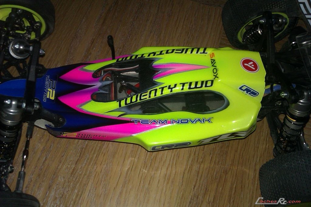 Buggy electrico de competicion Team Losi Racing 22 con carroceria rosa y verde vista desde arriba sobre suelo de madera