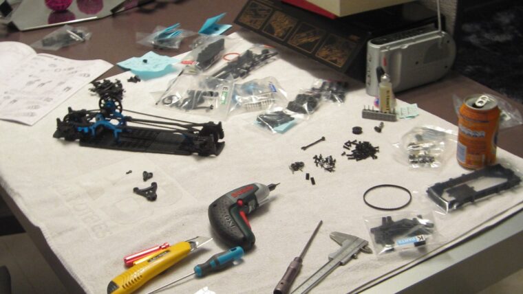 Mesa de trabajo con atornillador, calibre, cúter, tornillería y piezas de chasis de coche RC