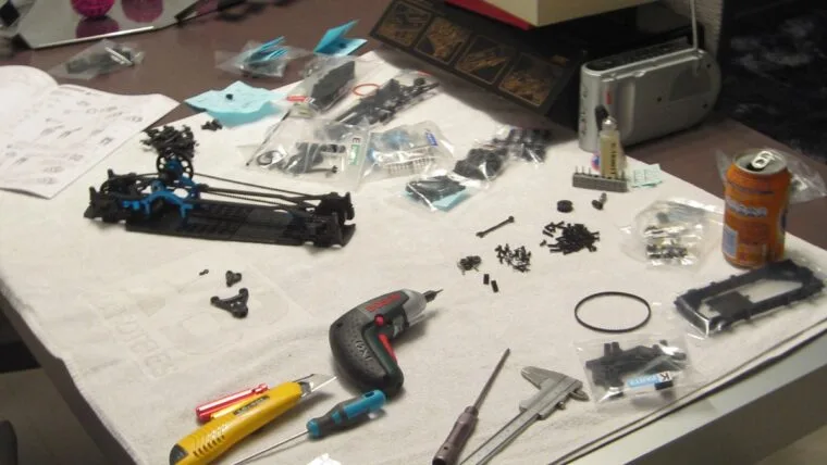 Mesa de trabajo con atornillador, calibre, cúter, tornillería y piezas de chasis de coche RC