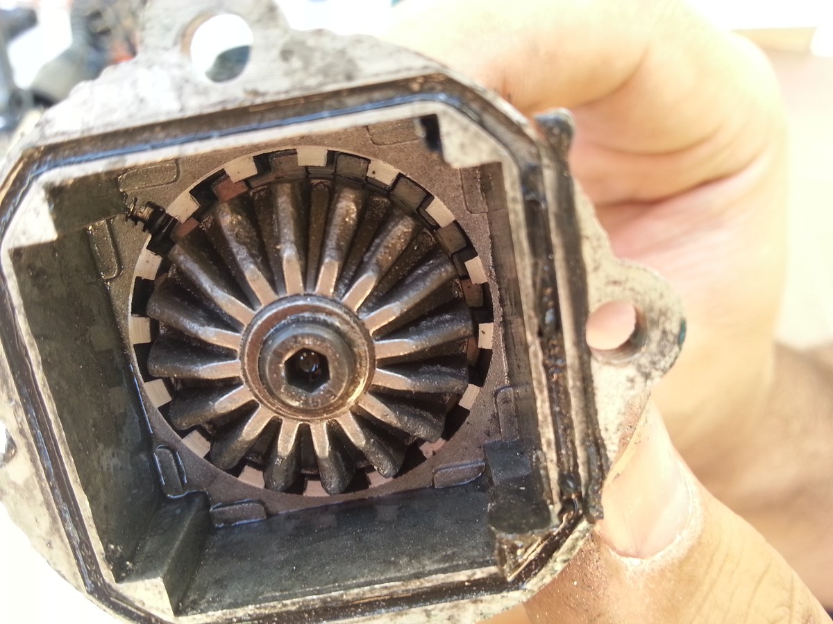 Piñón del diferencial de un coche RC cubierto de grasa y tierra, sostenido en la mano